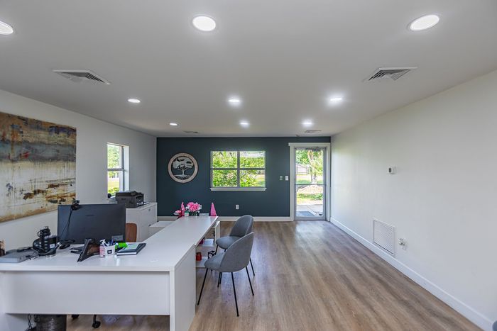 Modern office interior with white desk, dark teal accent wall, and wood-look flooring.