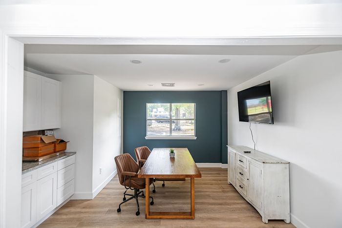 Modern office with blue accent wall, wooden table, chairs, and cabinets.