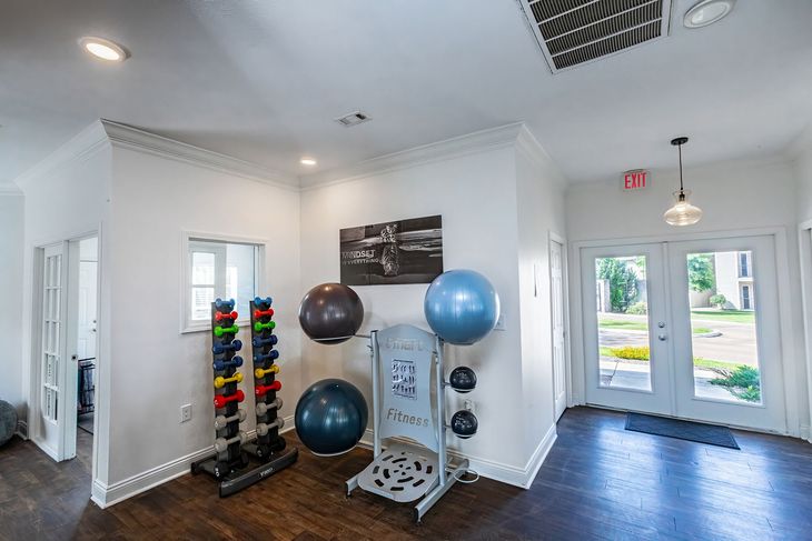Gym interior with weights, exercise balls, and exit doors. Dark wood floors, white walls, bright lighting.