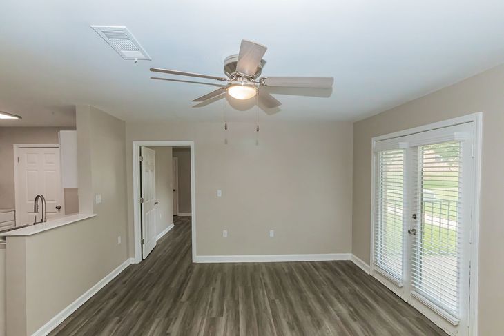 Living room with gray wood floors, neutral walls, sliding glass door, and ceiling fan.