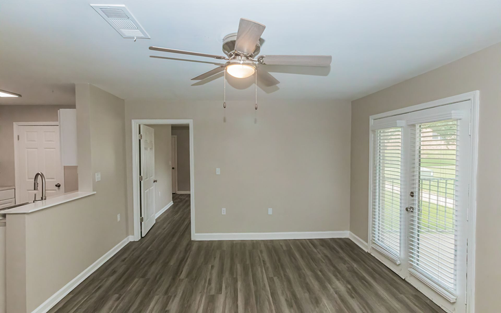 Living room with gray wood floors, neutral walls, sliding glass door, and ceiling fan.