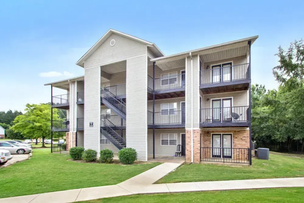 Apartment building with beige siding, black balconies, brick base, and green lawn.