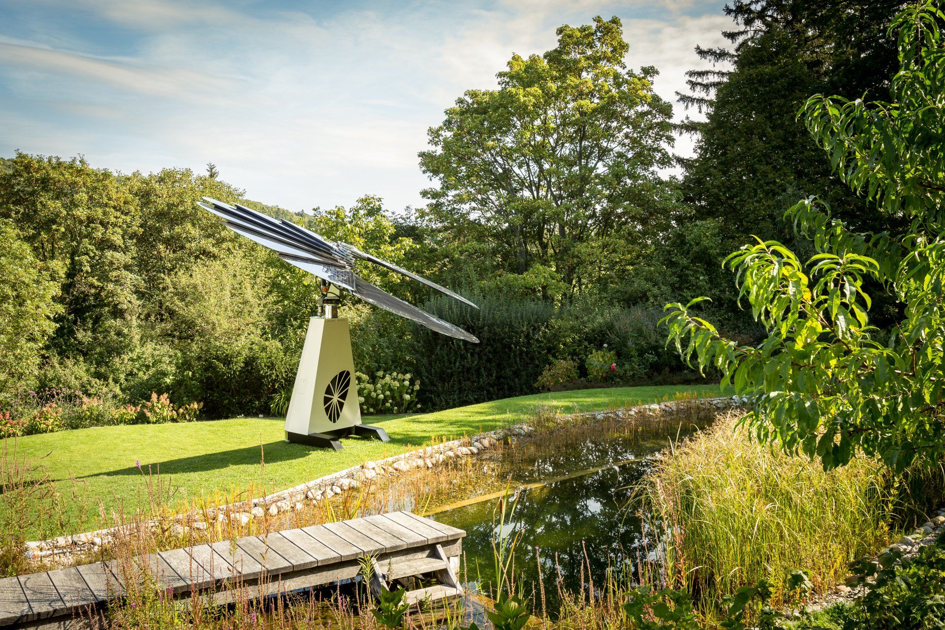 A large solar panel is sitting in the middle of a lush green field next to a pond.
