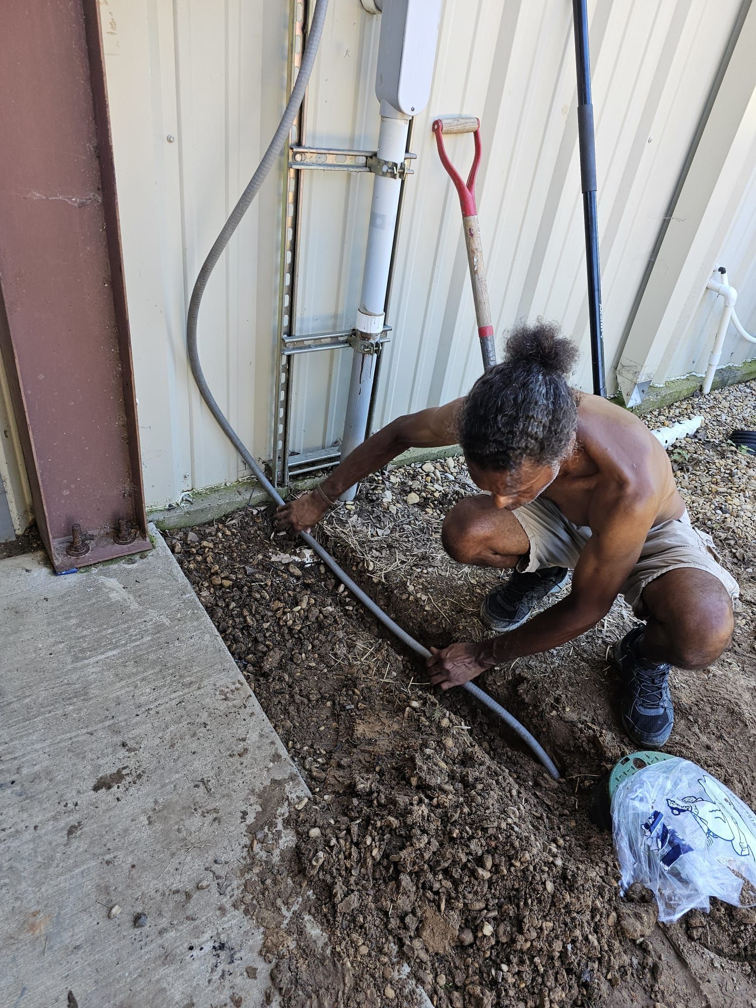 A man is kneeling down in the dirt working on a pipe.