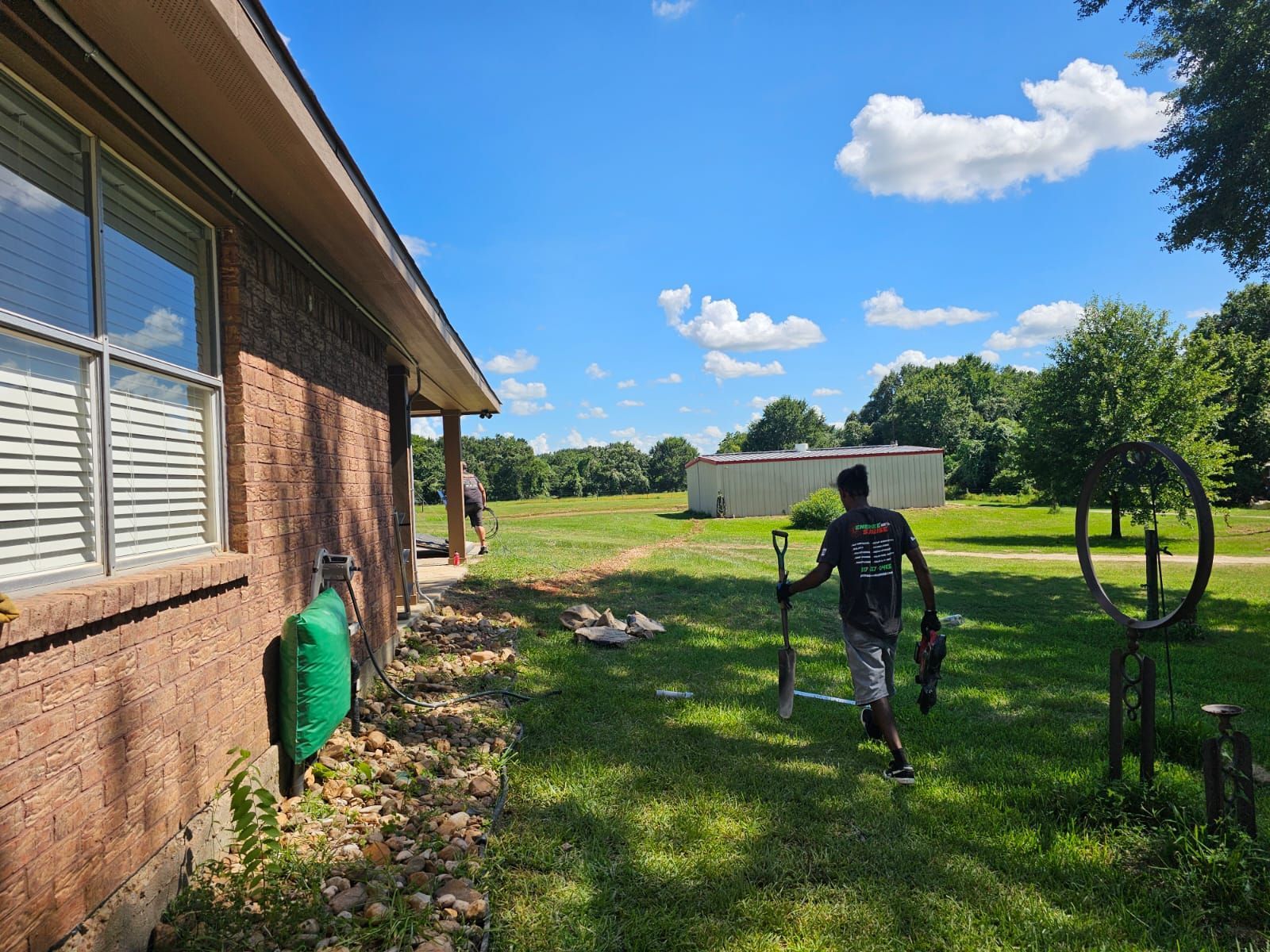 A man is standing in front of a house holding a shovel.