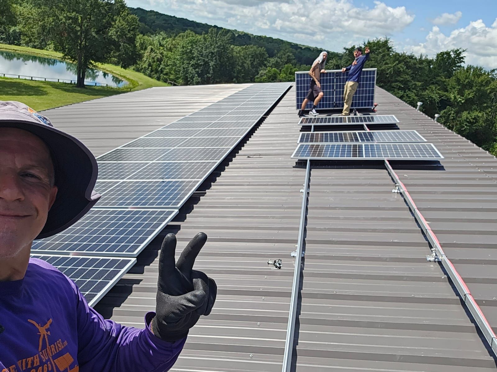 A man is giving a thumbs up in front of a row of solar panels on a roof.