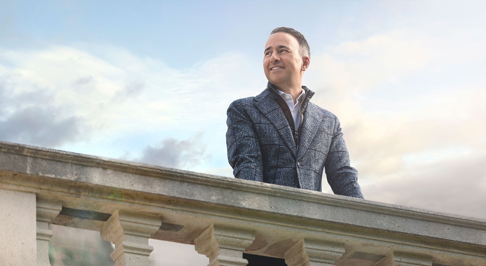 Ein Mann steht auf einem Balkon und schaut in den Himmel.