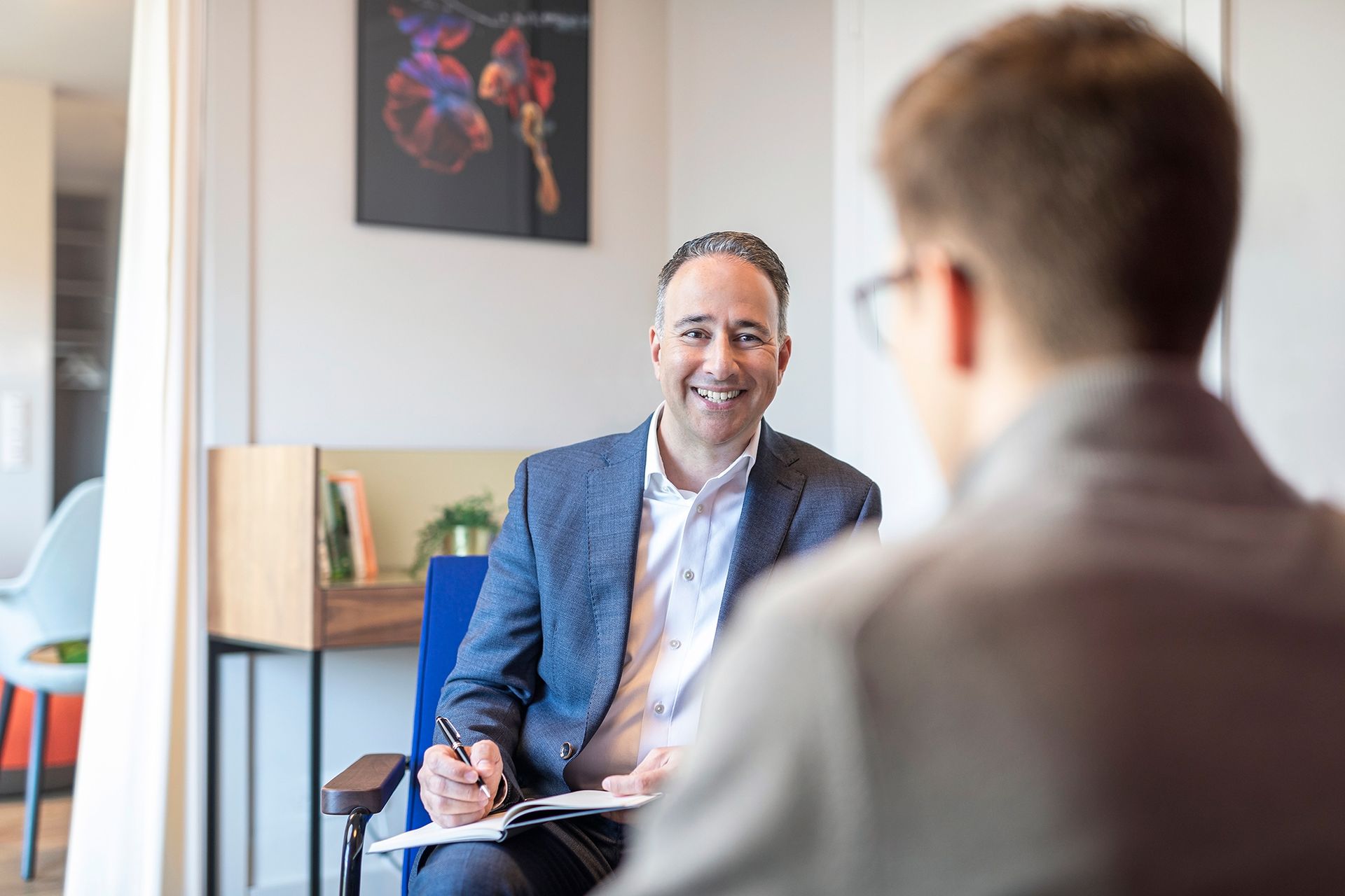 Ein Mann im Anzug sitzt auf einem Stuhl und unterhält sich mit einem anderen Mann.