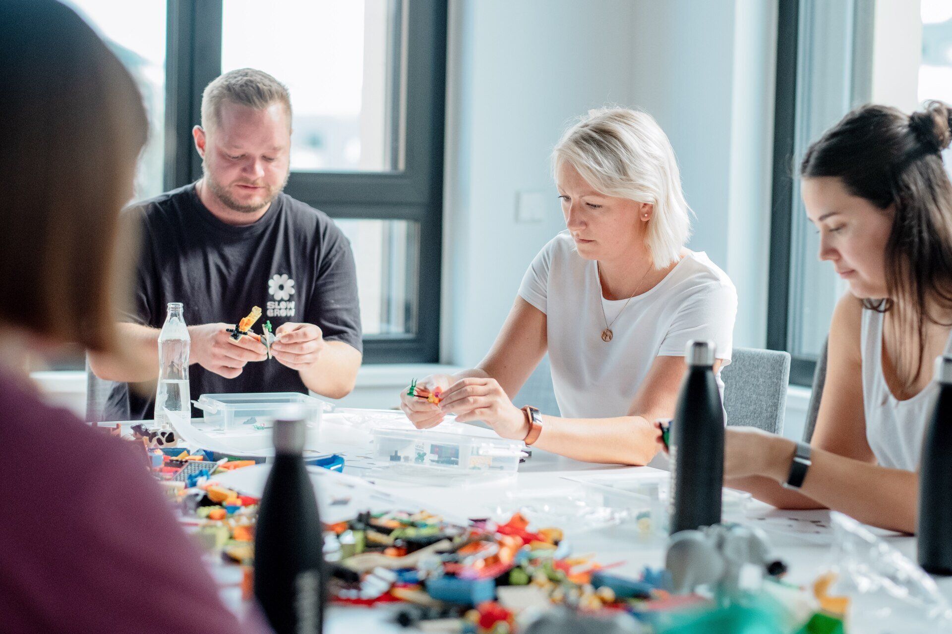 A group of people are sitting around a table playing with legos.