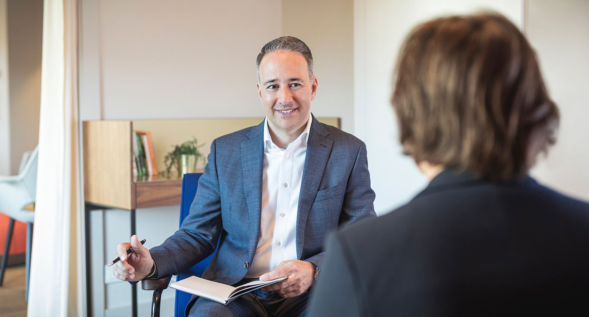 A man in a suit is sitting in a chair talking to a woman.