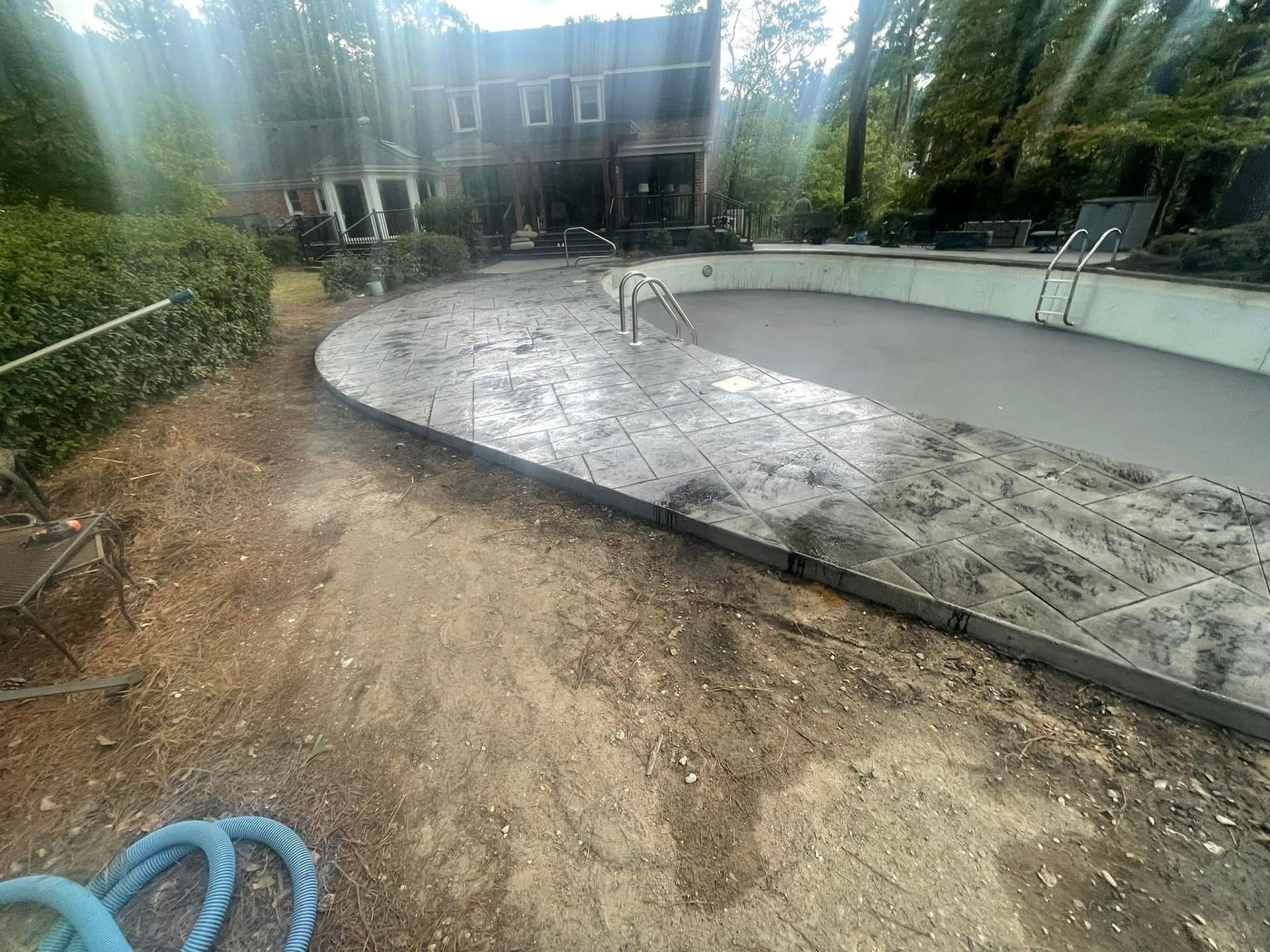 Newly poured concrete patio and pool edge. Backyard setting with a house in the background.