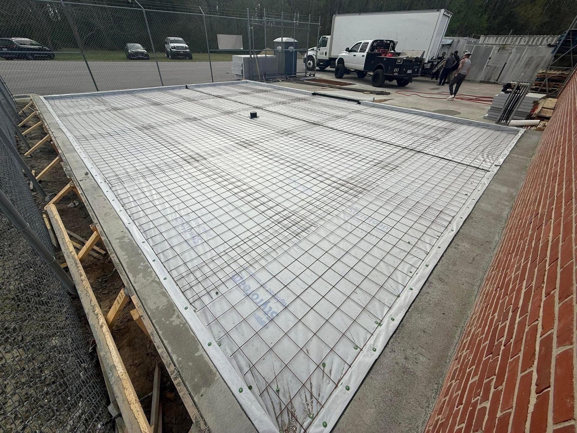 Concrete foundation with steel mesh, wooden supports, and brick wall. Construction site outdoors.