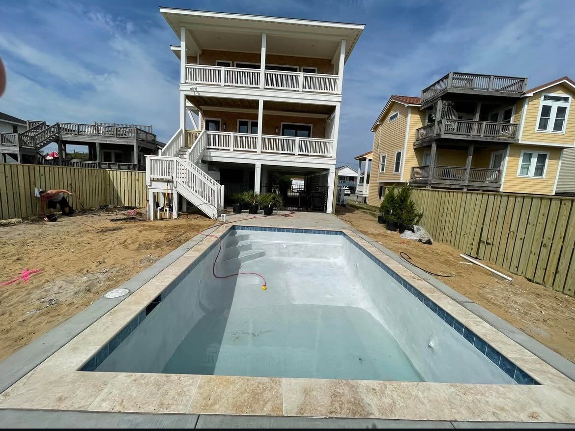 A rectangular swimming pool is under construction in front of a three-story house.