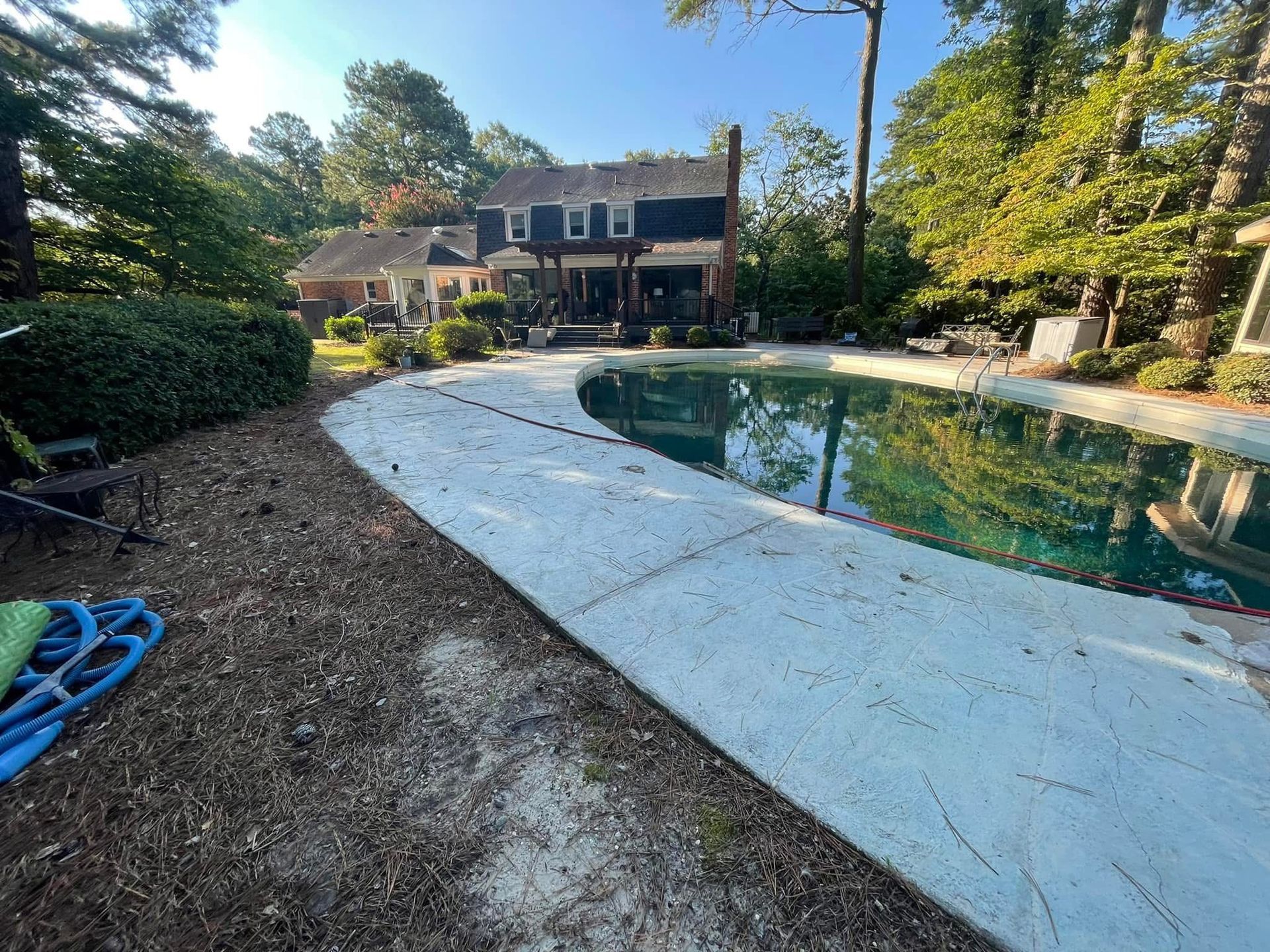 Backyard with pool, concrete walkway, and two-story house with trees.