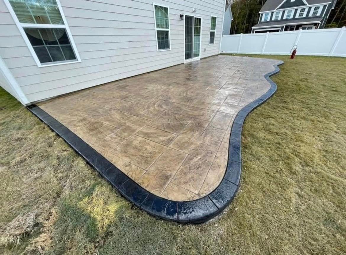 Stamped concrete patio with a dark border next to a beige house and green grass.