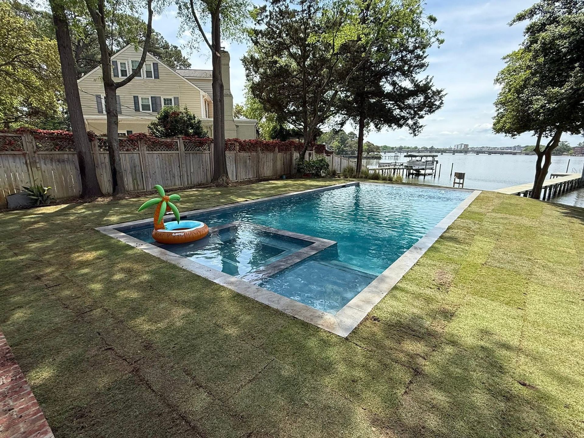 Pool with a floating palm tree, next to a waterfront home.