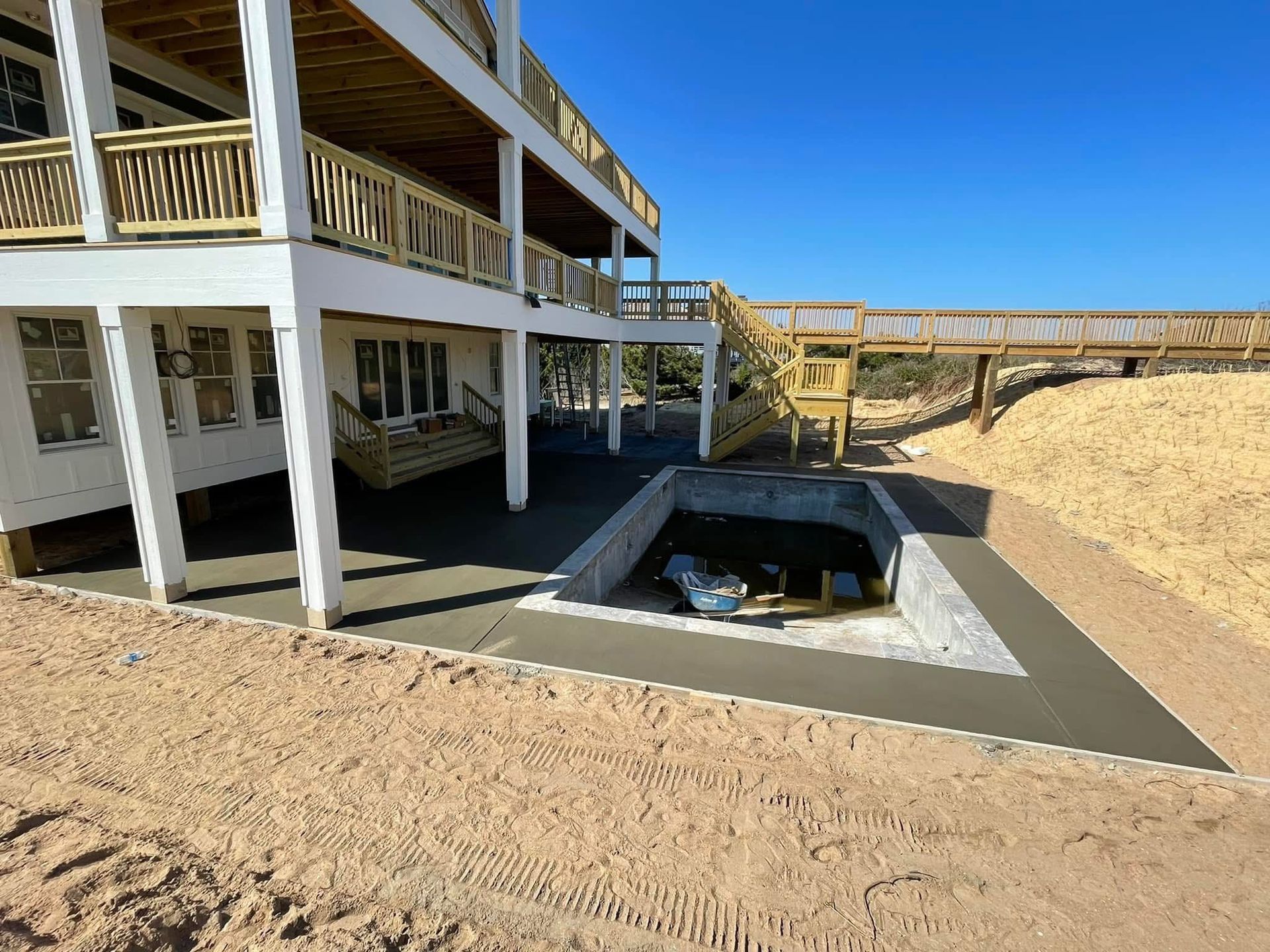 A two-story building with deck and concrete patio, next to a sandy hill.