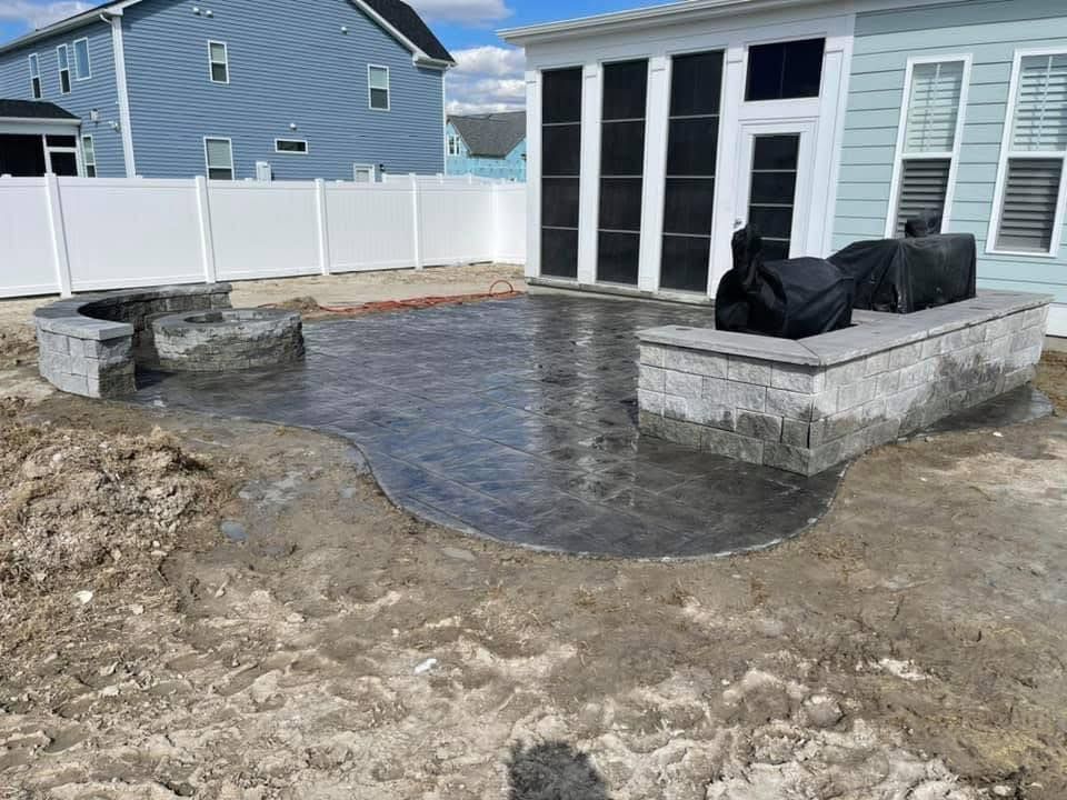 Outdoor patio with fire pit and built-in seating under construction. Grey concrete, dirt ground.