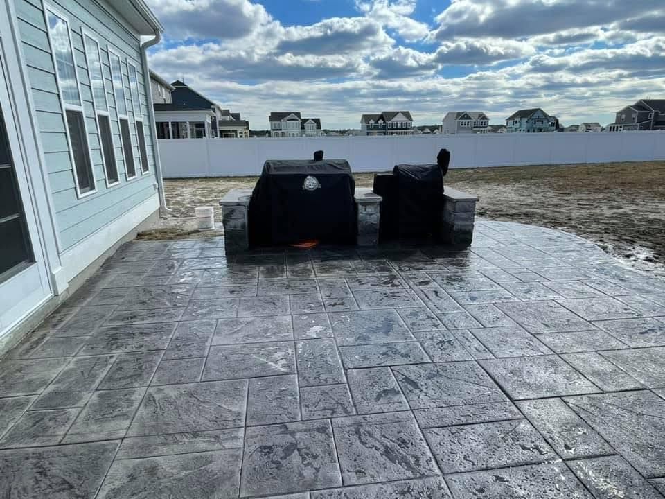 Stamped concrete patio with built-in grill and smoker, near a house with many windows. Overcast sky.
