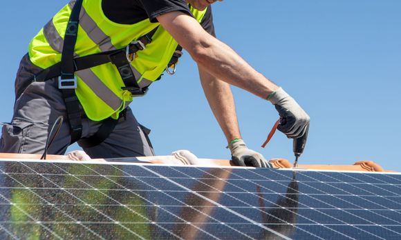 A technician fitting solar panels on a residential roof. A technician fitting solar panels on a residential roof.