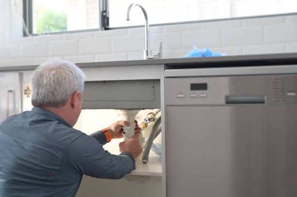 A man is fixing a sink in a kitchen with a screwdriver.