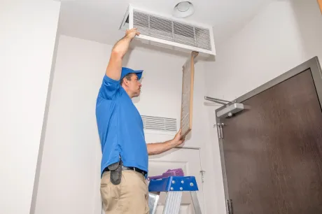 A man in a blue shirt is replacing an air filter in a doorway.