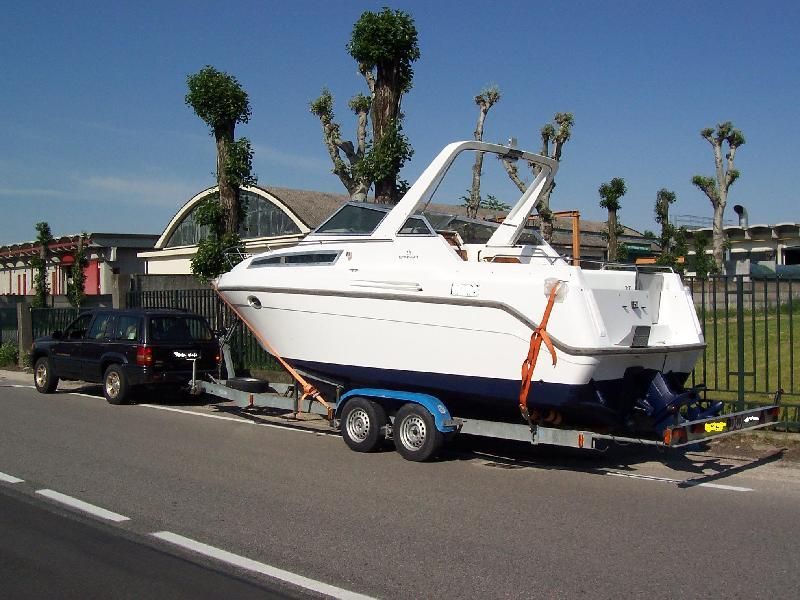 Una barca bianca su un rimorchio agganciato a un pick-up nero parcheggiato sul ciglio della strada.