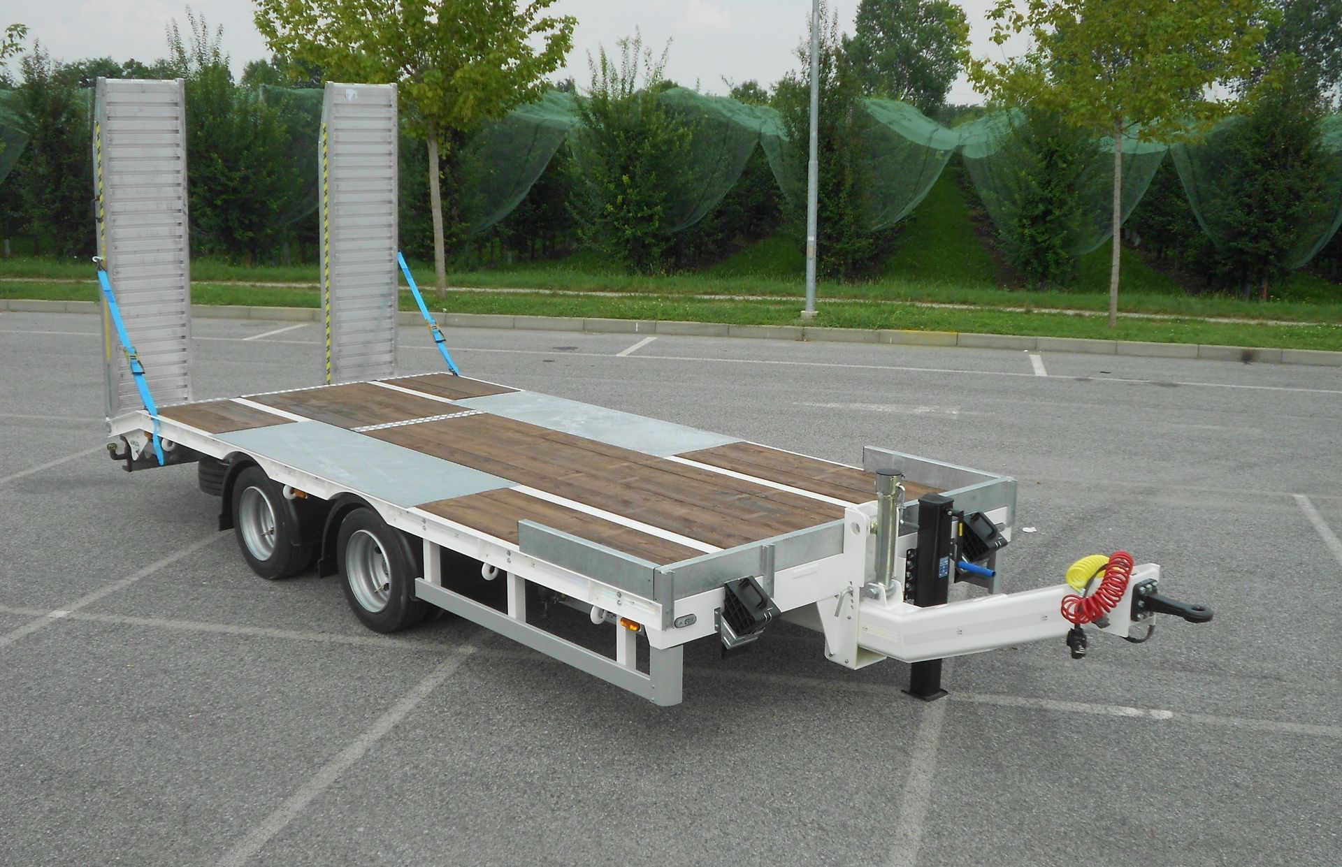 Rimorchio con pianale e rampe parcheggiato sull'asfalto.