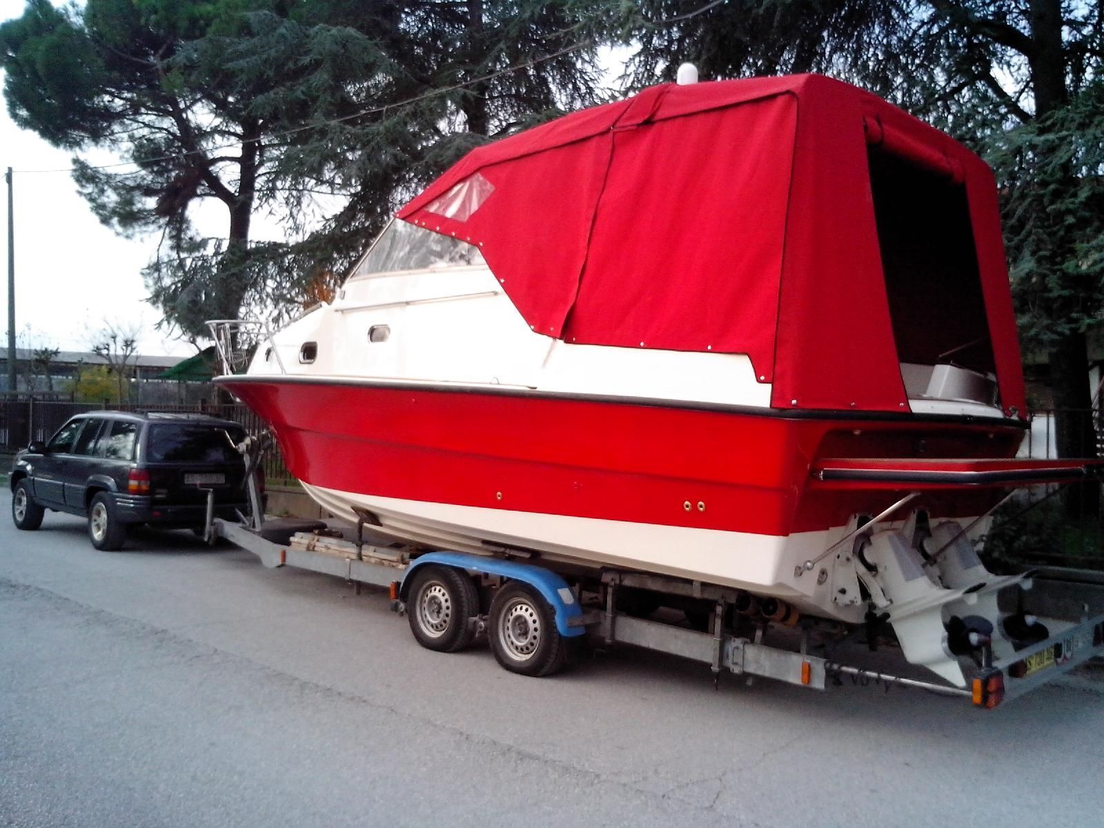 Barca rossa e bianca su un rimorchio, trainata da un SUV nero, con tettuccio rosso sollevato.