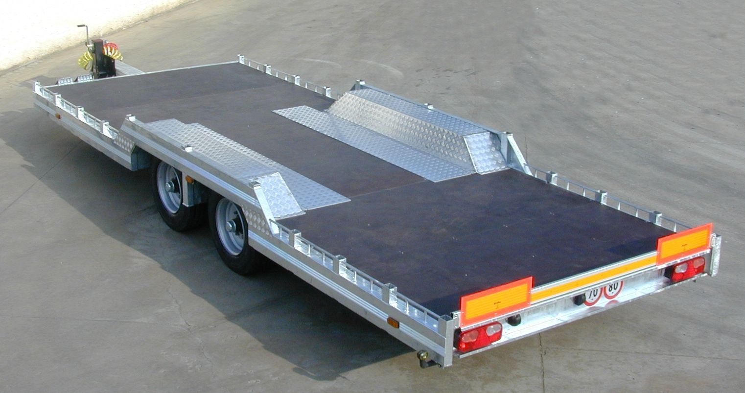 Un rimorchio per auto con pianale piatto, pavimento nero e telaio argentato, posizionato su una superficie grigia.
