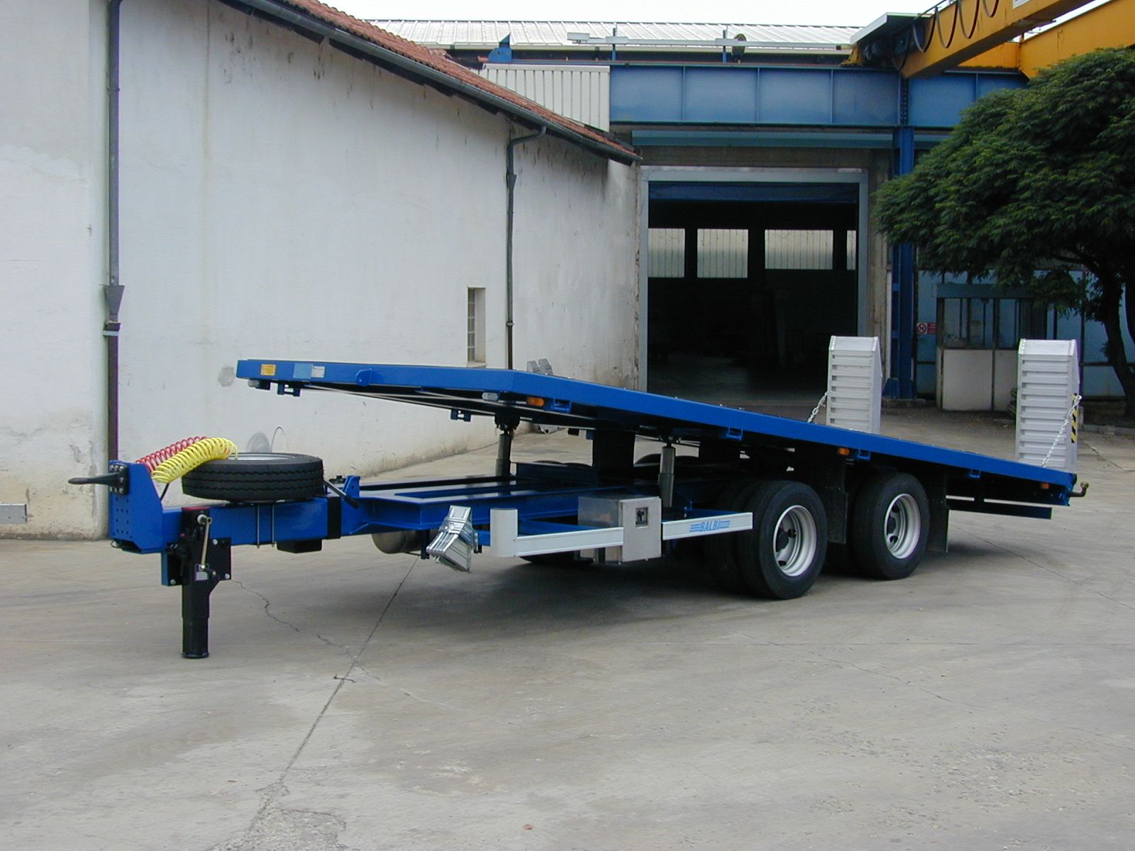 Rimorchio blu con pianale parcheggiato fuori da un edificio.