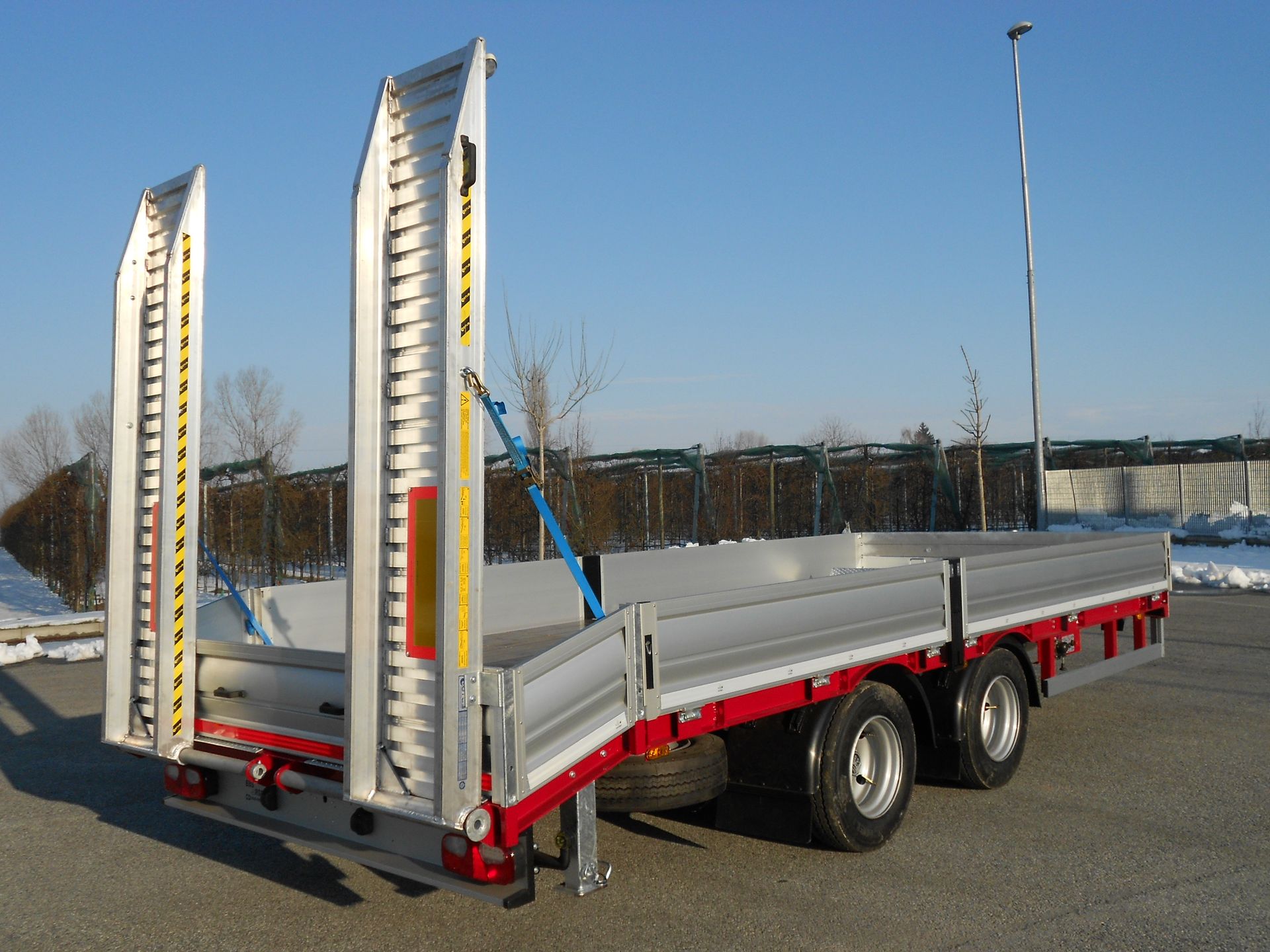 Rimorchio a pianale con rampe in alluminio, dettagli rossi e due assi.