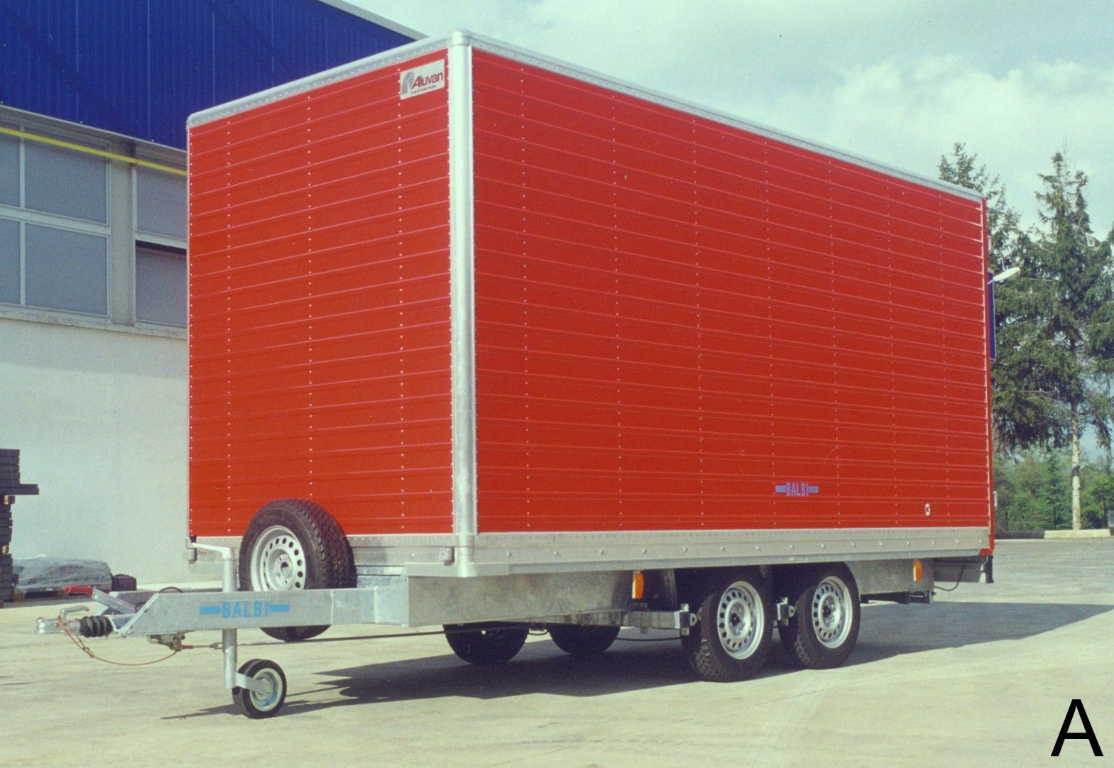 Rimorchio rosso chiuso con tre assi e gancio anteriore, parcheggiato all'aperto.