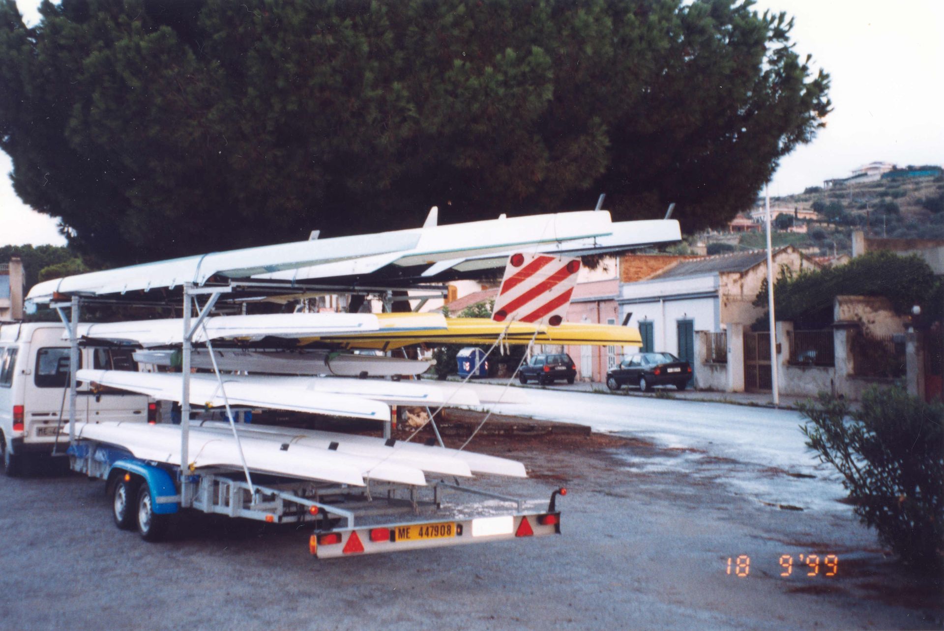Rimorchio per barche con scafi da corsa parcheggiato su una strada vicino a una città costiera.