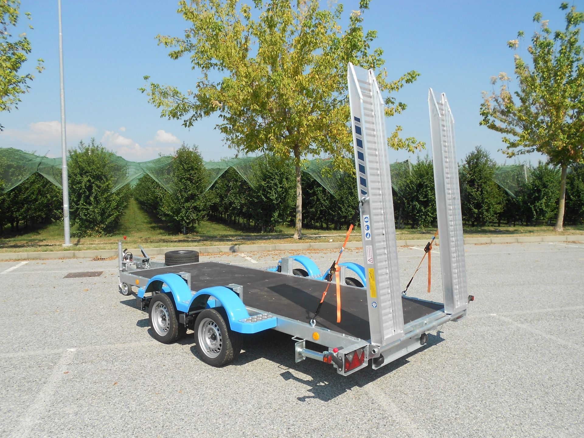 Rimorchio con pianale, parafanghi blu, rampe di carico, parcheggiato all'aperto.