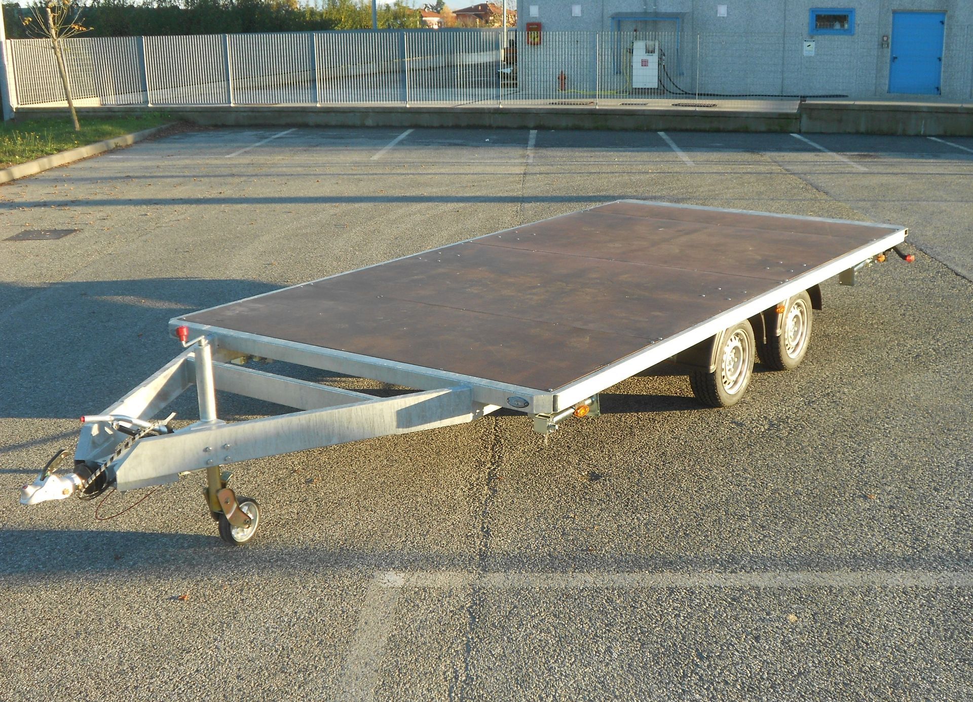 Rimorchio con pianale ribassato su un parcheggio asfaltato, con un pianale marrone e un gancio.