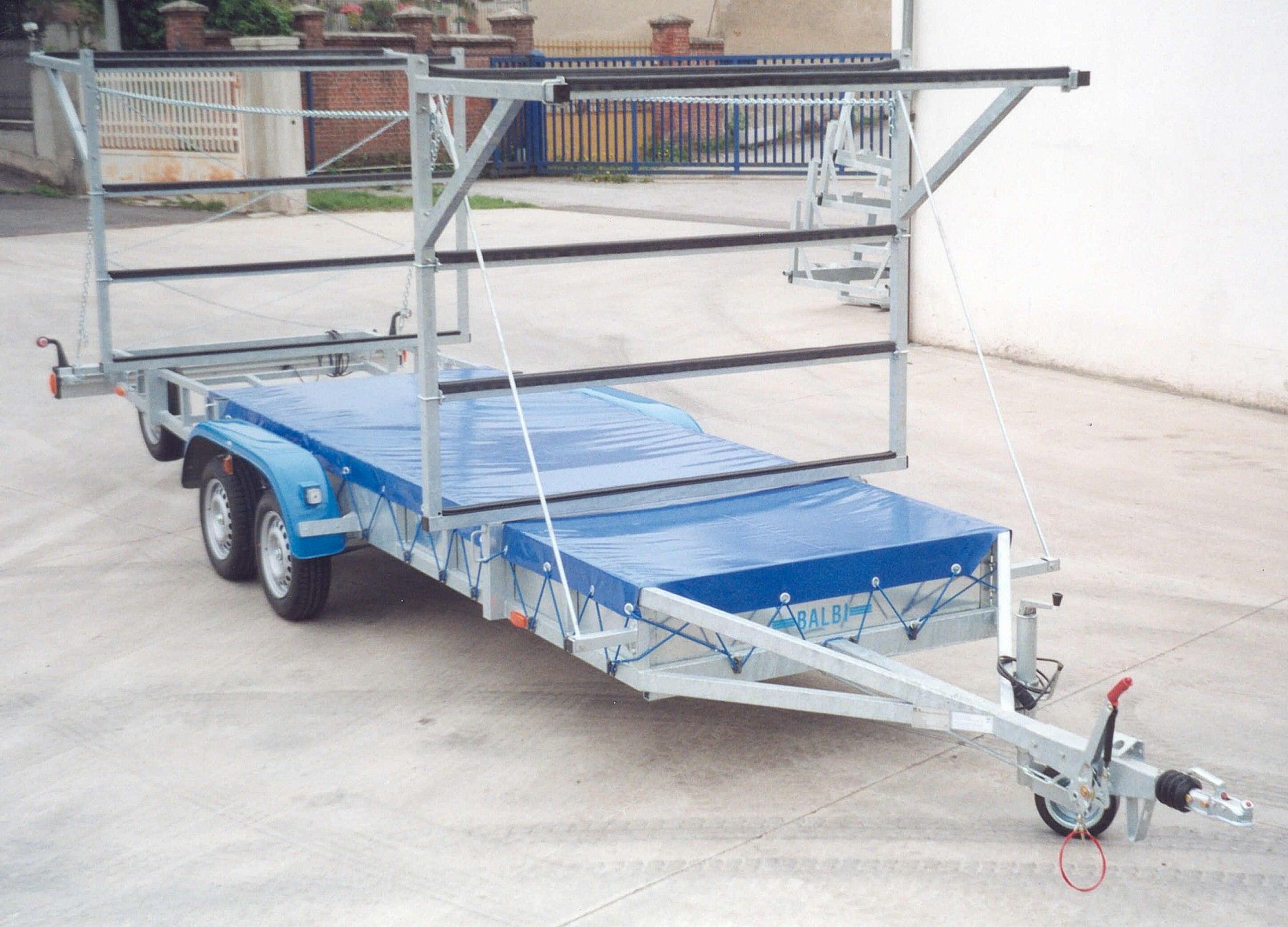 Rimorchio con telone blu e telaio superiore per il trasporto di oggetti lunghi.