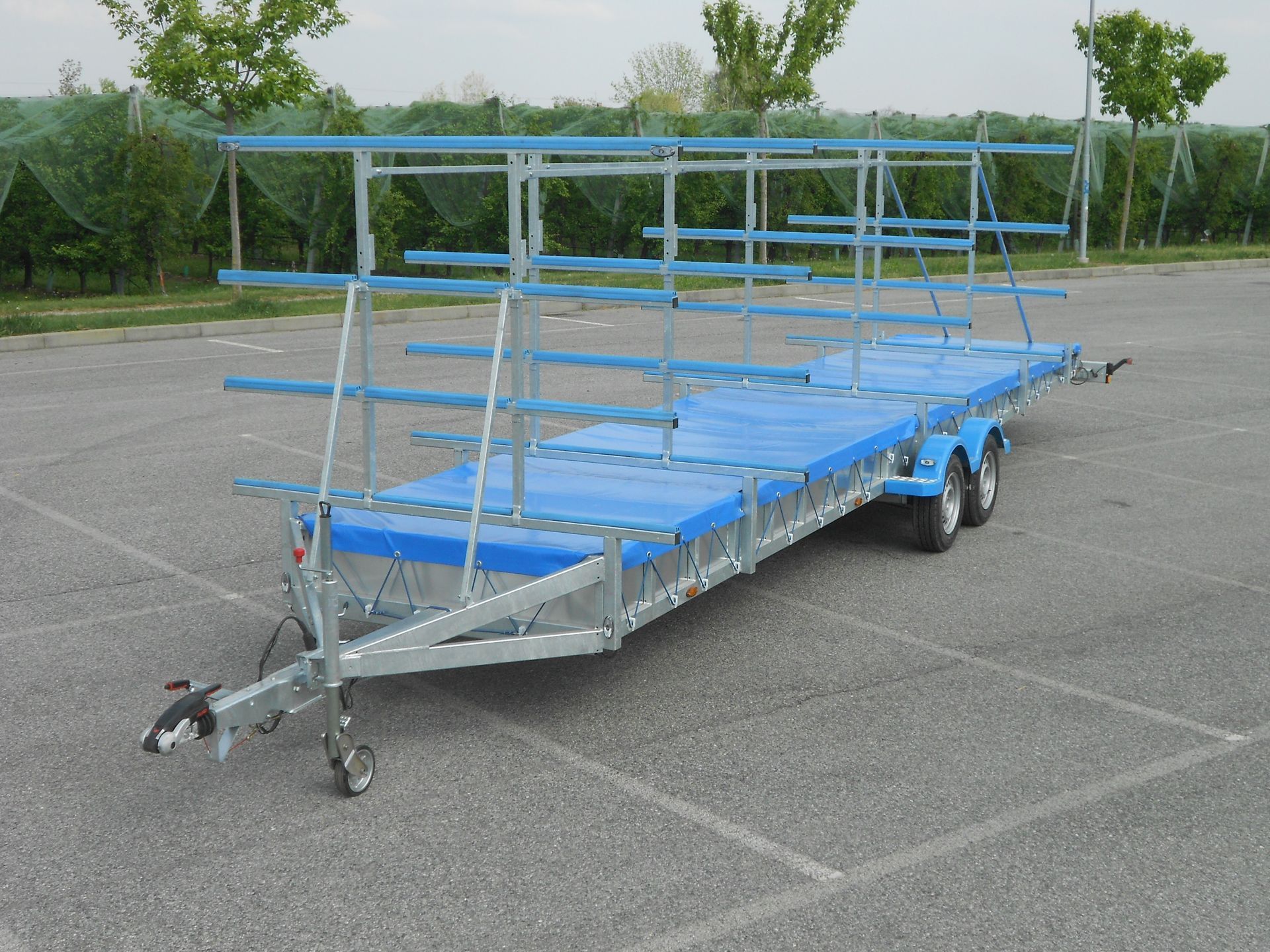 Rimorchio blu e argento con più barre orizzontali, parcheggiato sull'asfalto.