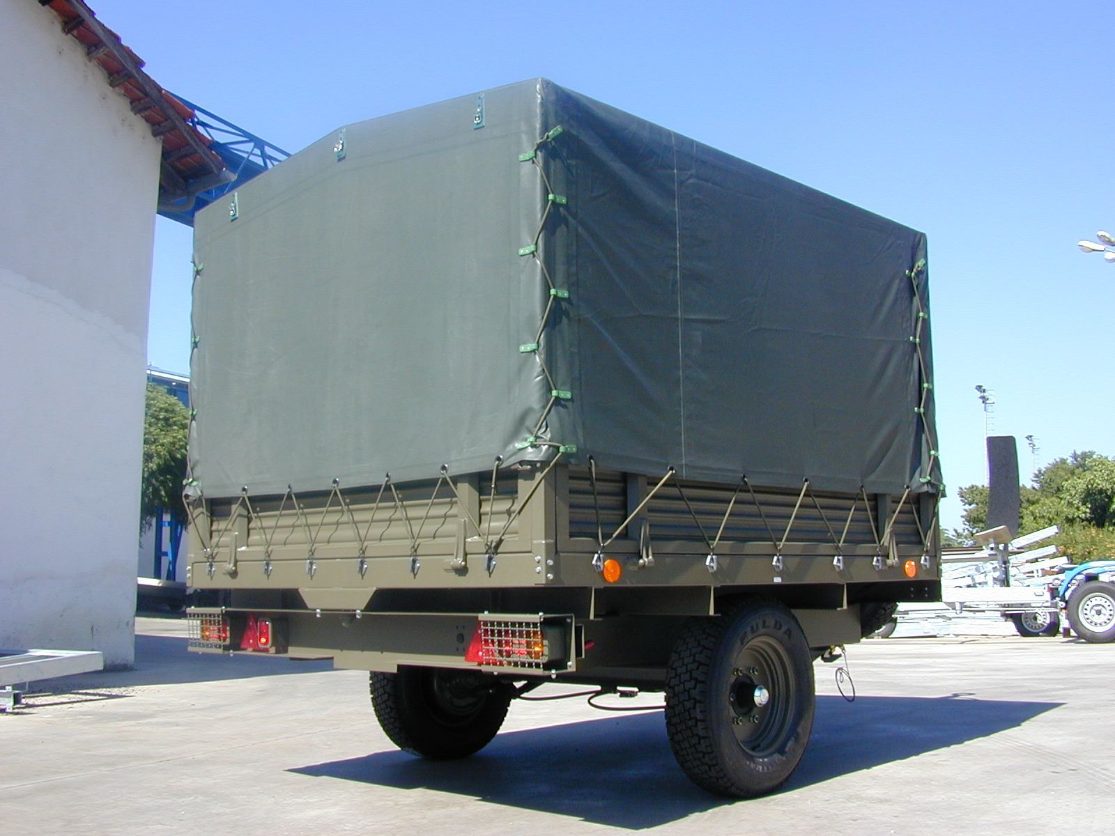 Rimorchio militare con copertura in tela verde e pneumatici neri, situato in un'area esterna.