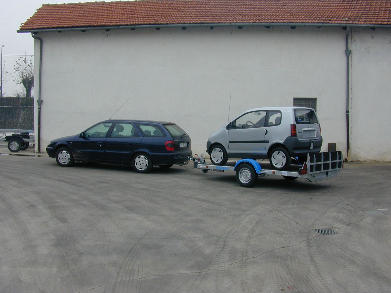 Una station wagon blu con a bordo un rimorchio e un'auto argentata, parcheggiata in un parcheggio.