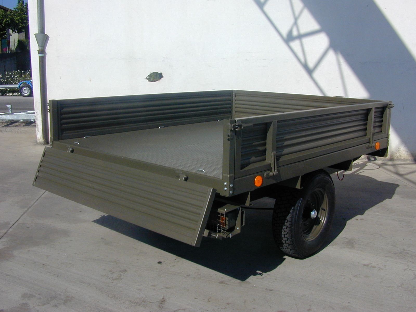 Rimorchio a pianale color verde oliva su una superficie di cemento, con un solo pneumatico e fanale posteriore visibile.