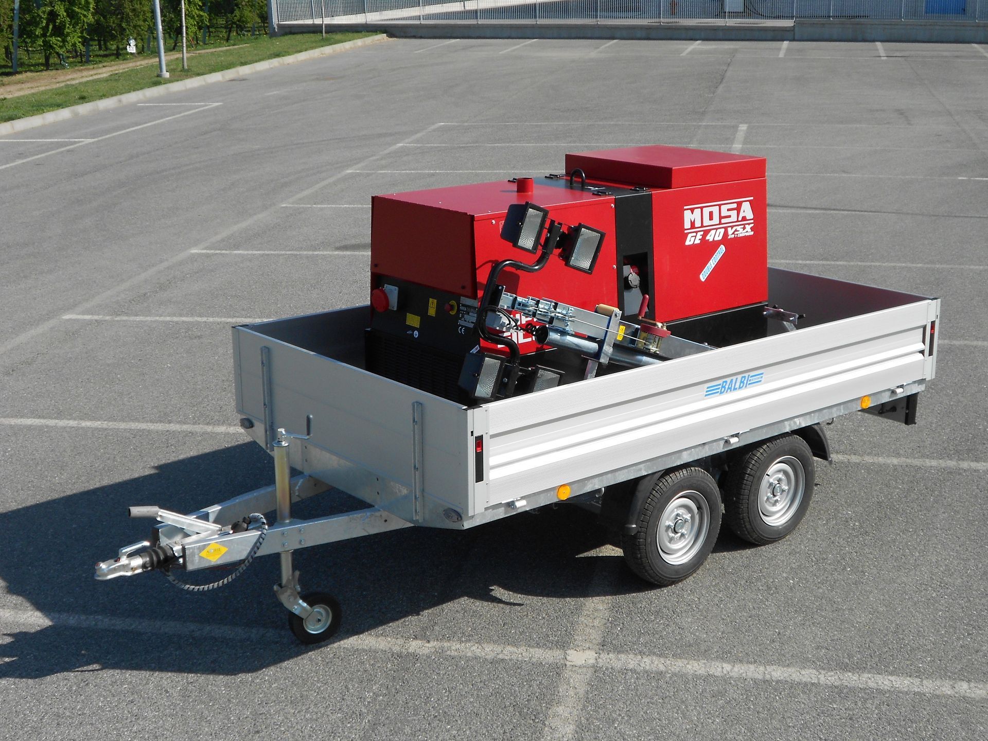 Macchina industriale rossa su un rimorchio grigio in un piazzale asfaltato.