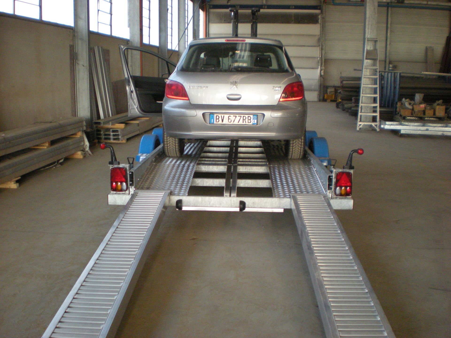 Un'auto argentata su un rimorchio blu per il trasporto di auto all'interno di un edificio con una porta aperta.
