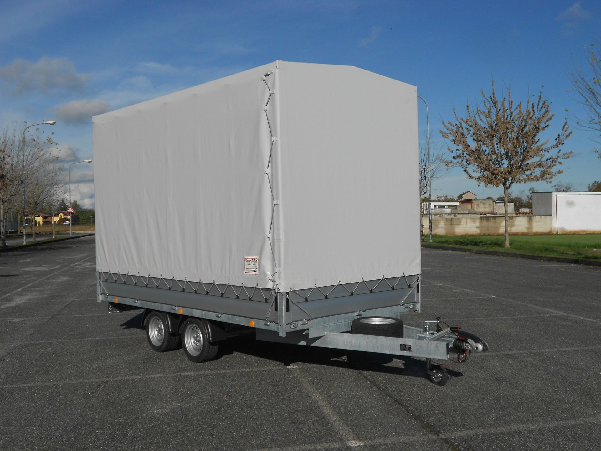 Rimorchio grigio chiuso sull'asfalto, parcheggiato in una giornata di sole.