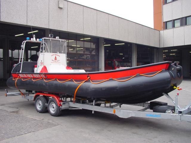 Una barca di salvataggio rossa e nera su un rimorchio, di fronte a un edificio con le porte del garage aperte.