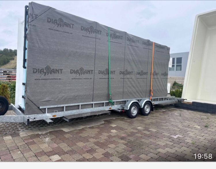 Un rimorchio che trasporta grandi materiali edili grigi, fissati con cinghie, è parcheggiato su una superficie di mattoni.