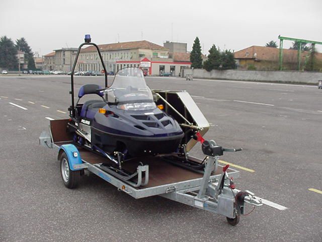 Motoslitta su rimorchio. Motoslitta blu con parabrezza e barra portatutto su un rimorchio a pianale, parcheggiata sull'asfalto.