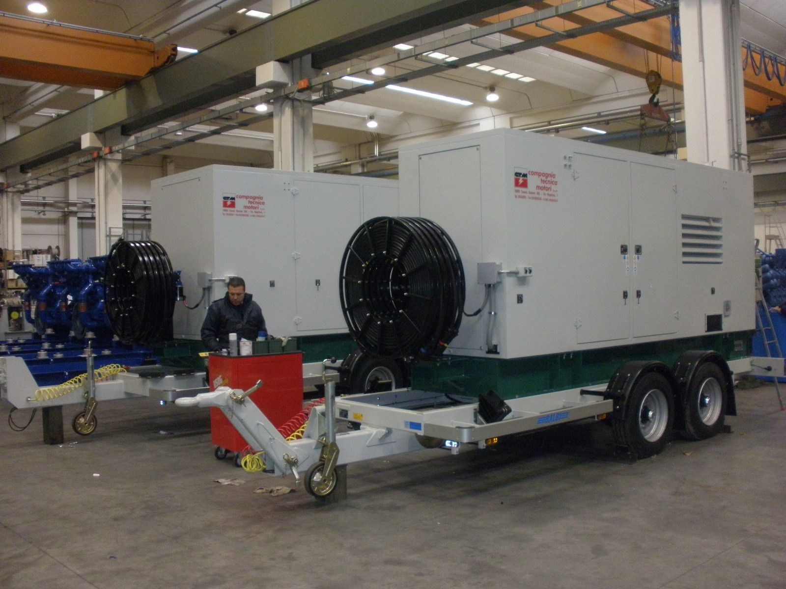 Due generatori industriali bianchi su rimorchi all'interno di un magazzino. Uomo seduto a un tavolo.