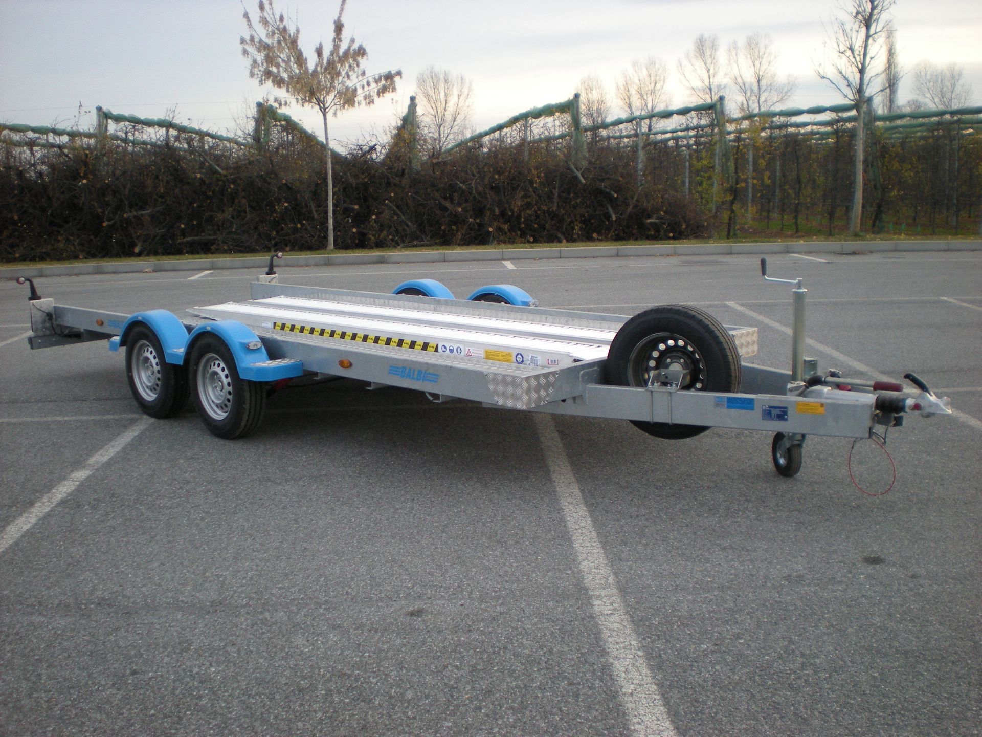 Rimorchio per auto in un parcheggio. Argento e blu con ruota di scorta.