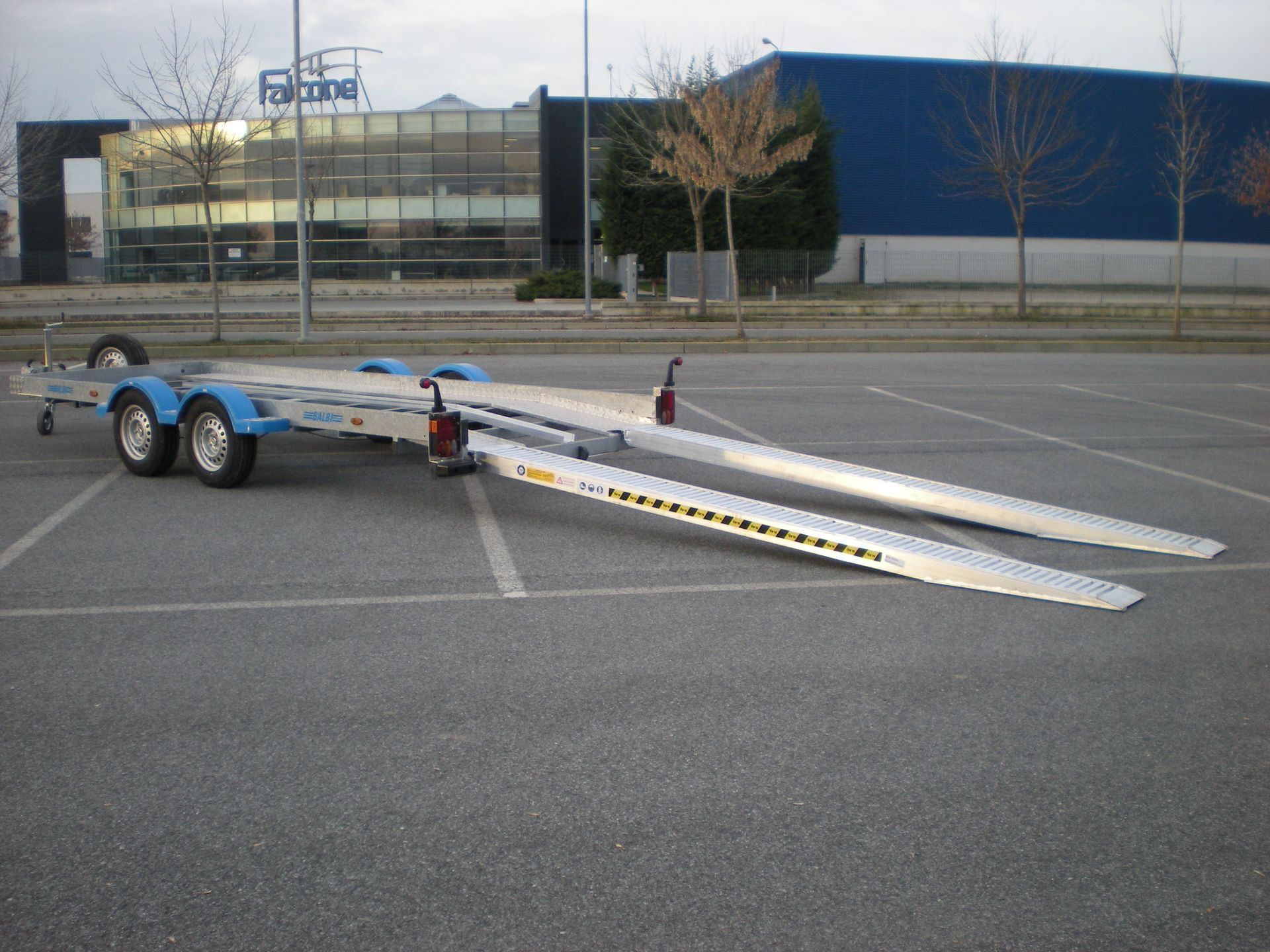 Rimorchio blu con rampe estese, parcheggiato su un piazzale asfaltato. Sullo sfondo si vede un edificio.